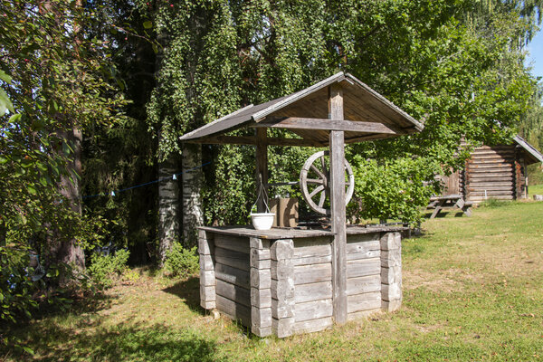 Ein rustikaler Holzwunschbrunnen mit Eimer, umgeben von Bäumen und Wiese.